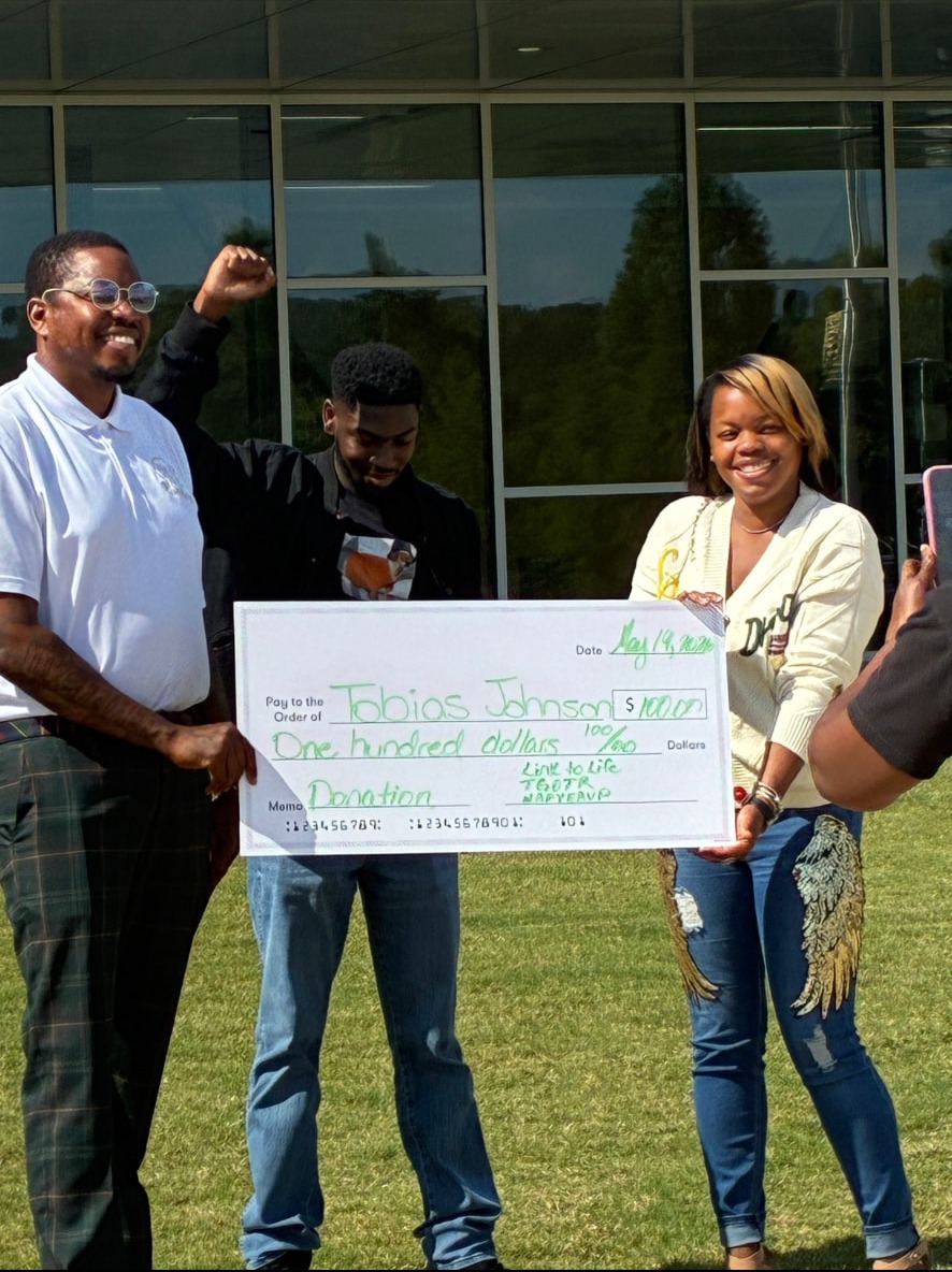 Tobias Johnson with community supporters holding a $100 check outdoors